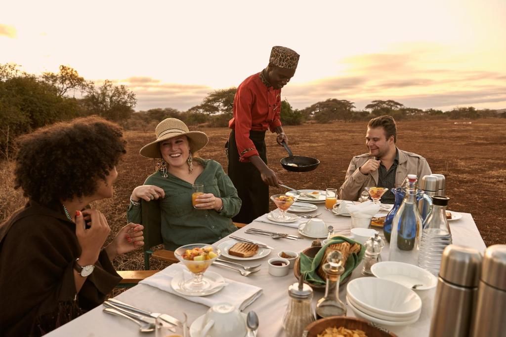 A group of people dining outdoors at a table set with various dishes, utensils, and a bottle.