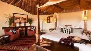 A room with a bed, a desk, a chair, a fireplace, and a ceiling with a thatched roof. - Tawi Lodge (Amboseli)