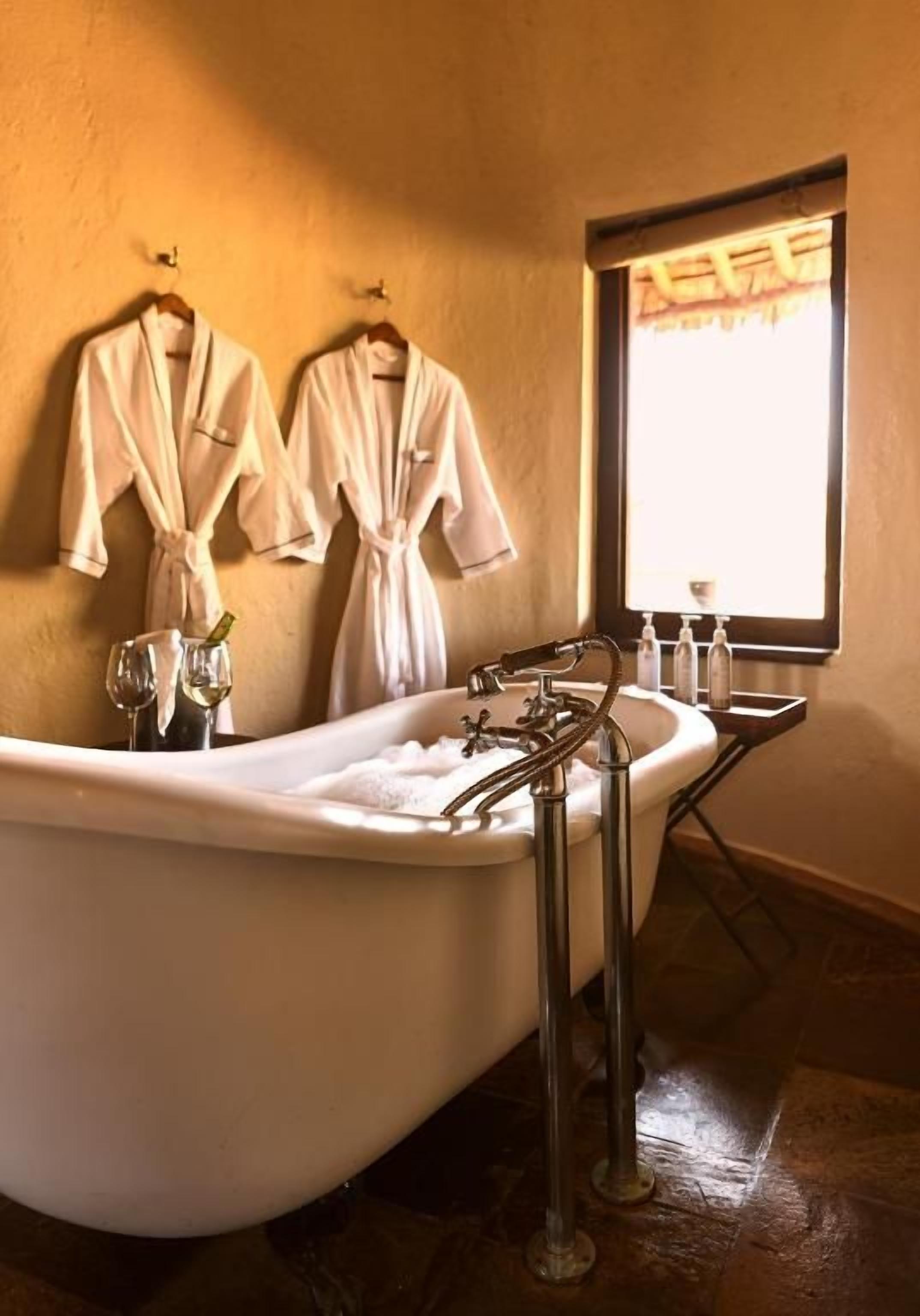 Un baño con una bañera independiente, dos albornoces blancos colgados en la pared y un ventanal con vistas.