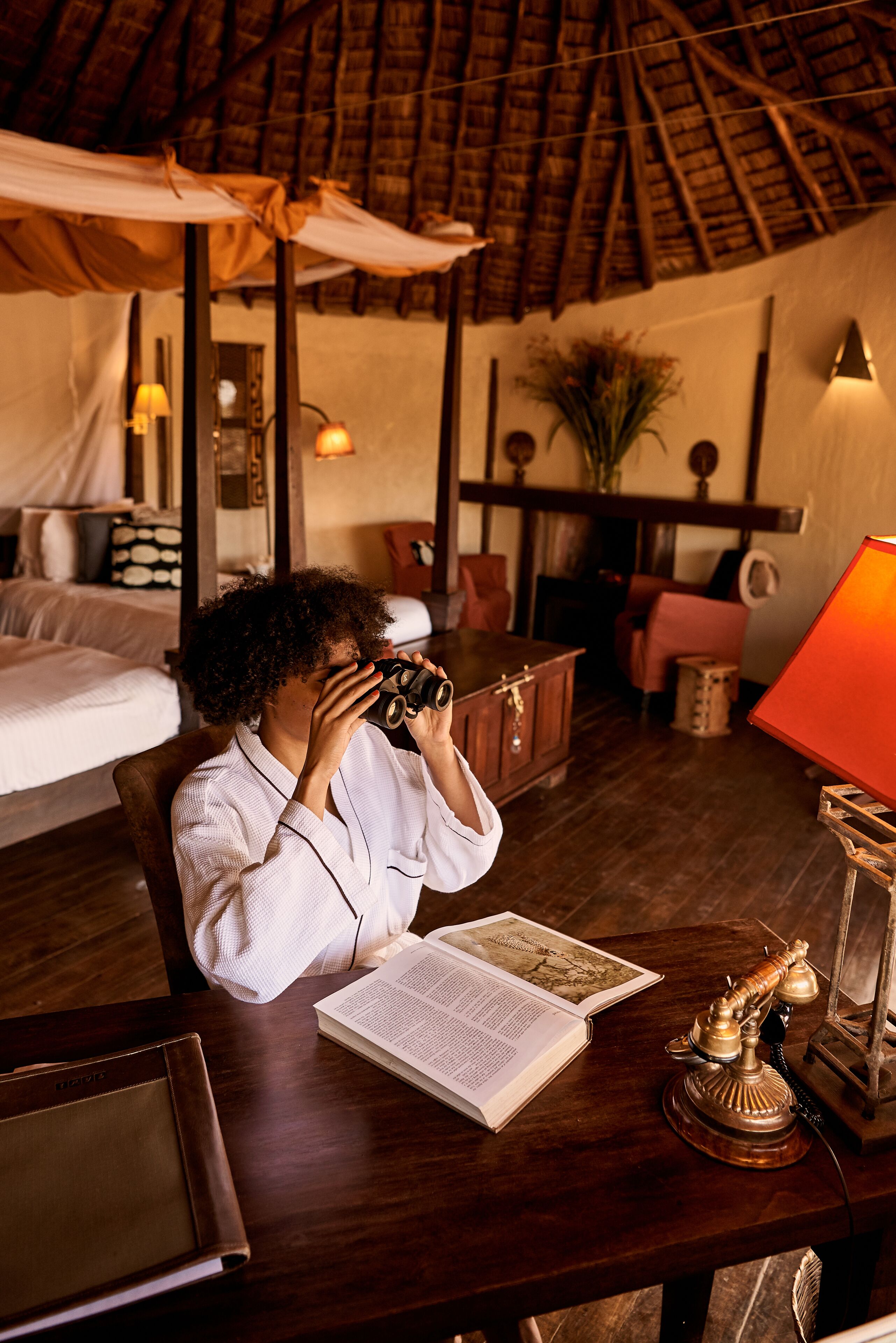 A room with a bed, a desk with a lamp, a telephone, and a book.