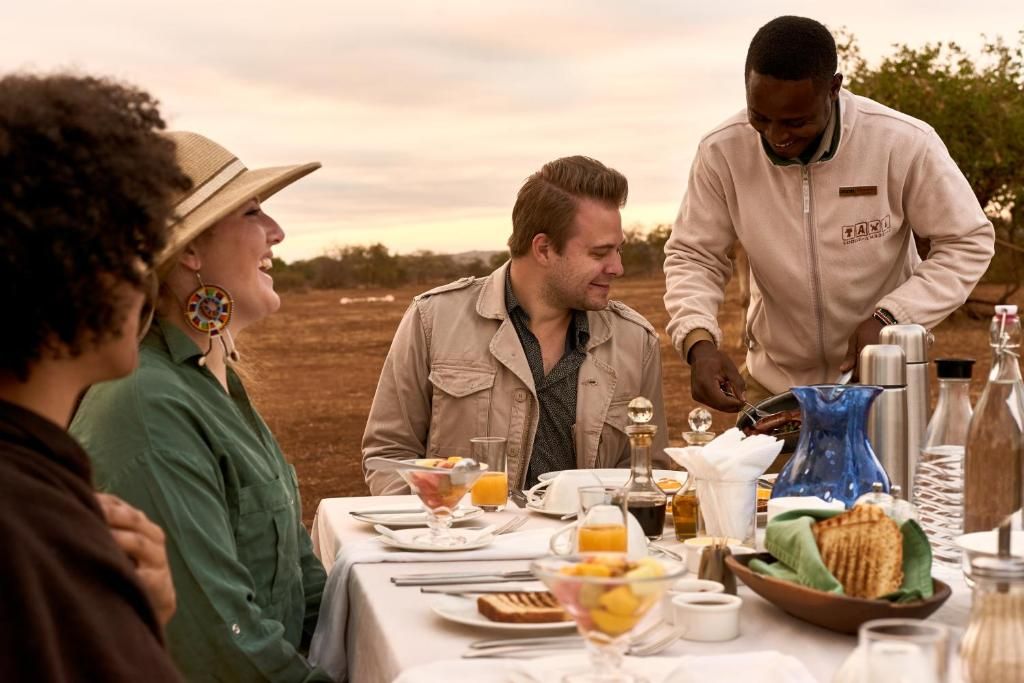 A group of people dining outdoors with a table set for breakfast, including various dishes and beverages.