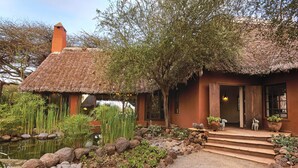 A rustic house with a thatched roof, a pond, and a garden with rocks and plants. - Tawi Lodge (Amboseli)