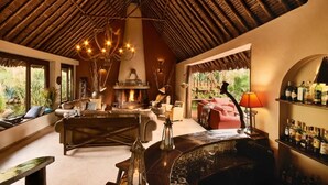 A cozy lounge area with a fireplace, seating, and a bar with bottles. - Tawi Lodge (Amboseli)