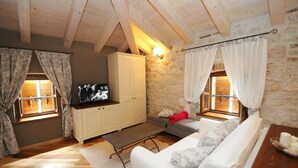 A cozy room with a stone wall, wooden beams, a white sofa, a television, and a bench. - Bed & Breakfast Korta Gira (Porec)