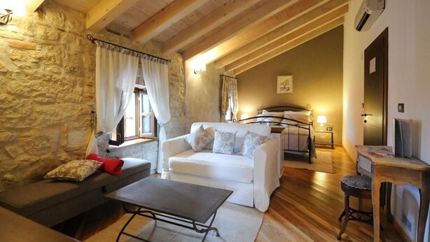 A cozy room with a stone wall, wooden beams, a white sofa, a small table, and a bed with a headboard. - Bed & Breakfast Korta Gira (Porec)