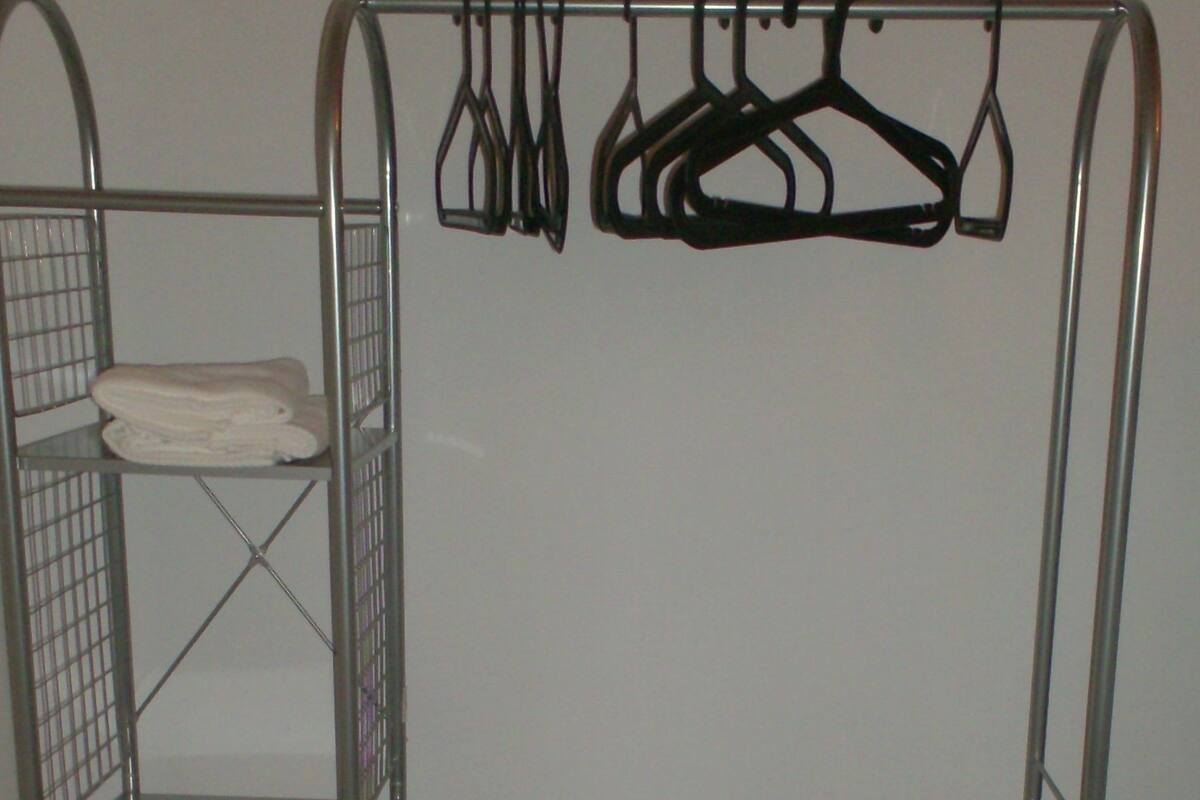 A metal shelf unit with a folded towel on the top shelf and several hangers on the right side.