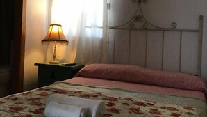 Un dormitorio con cama, mesita de noche, lámpara y ventana con cortinas.