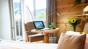 A hotel room with a bed, a laptop on a table, a chair, a vase of flowers, and a bottle of wine. - Hotel Sonne (Wildhaus-Alt St. Johann)