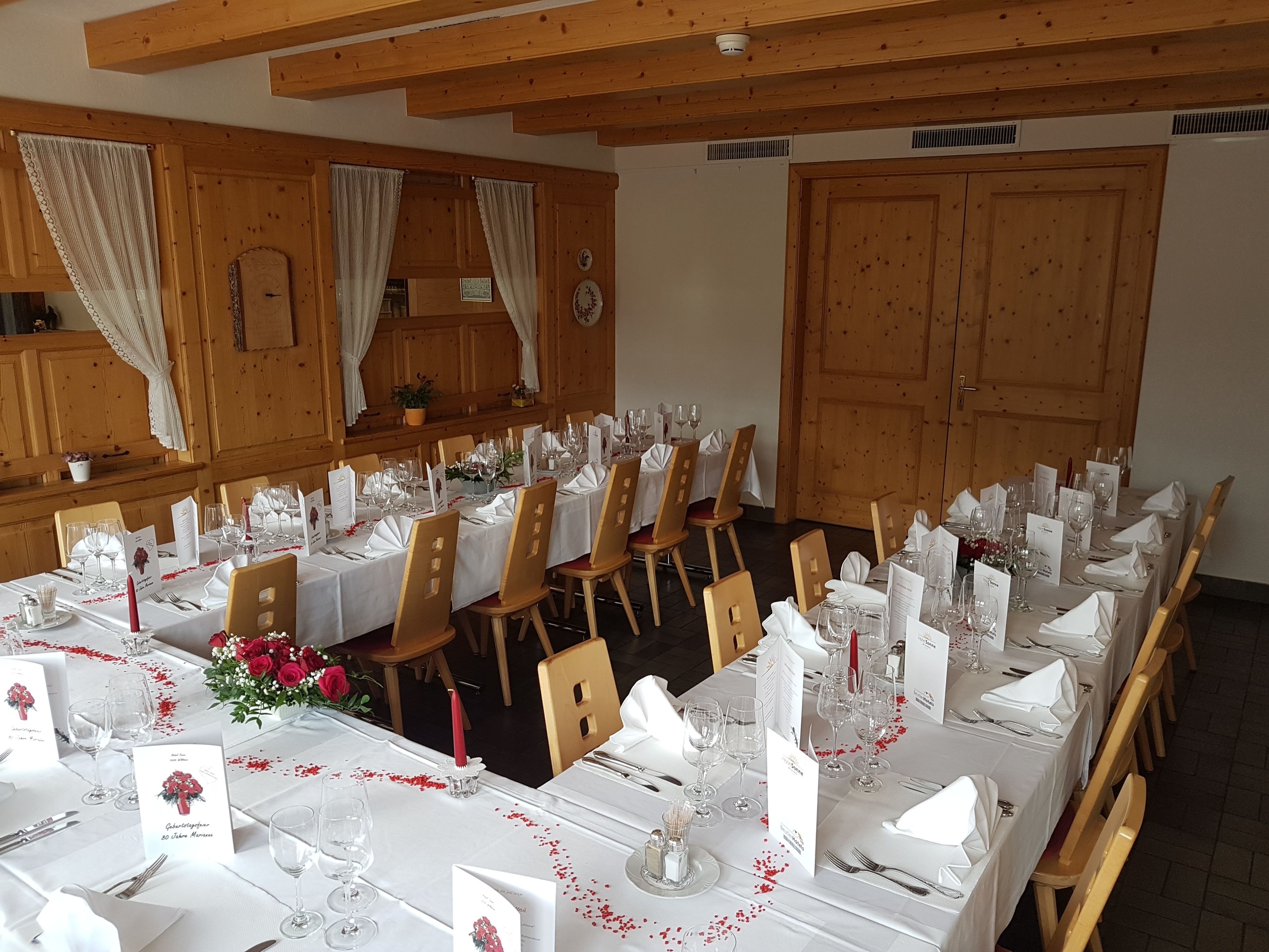 A banquet hall with long tables set for a formal event, wooden paneling on the walls, and a large door.