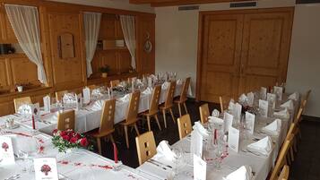 A banquet hall with long tables set for a formal event, wooden paneling on the walls, and a large door.