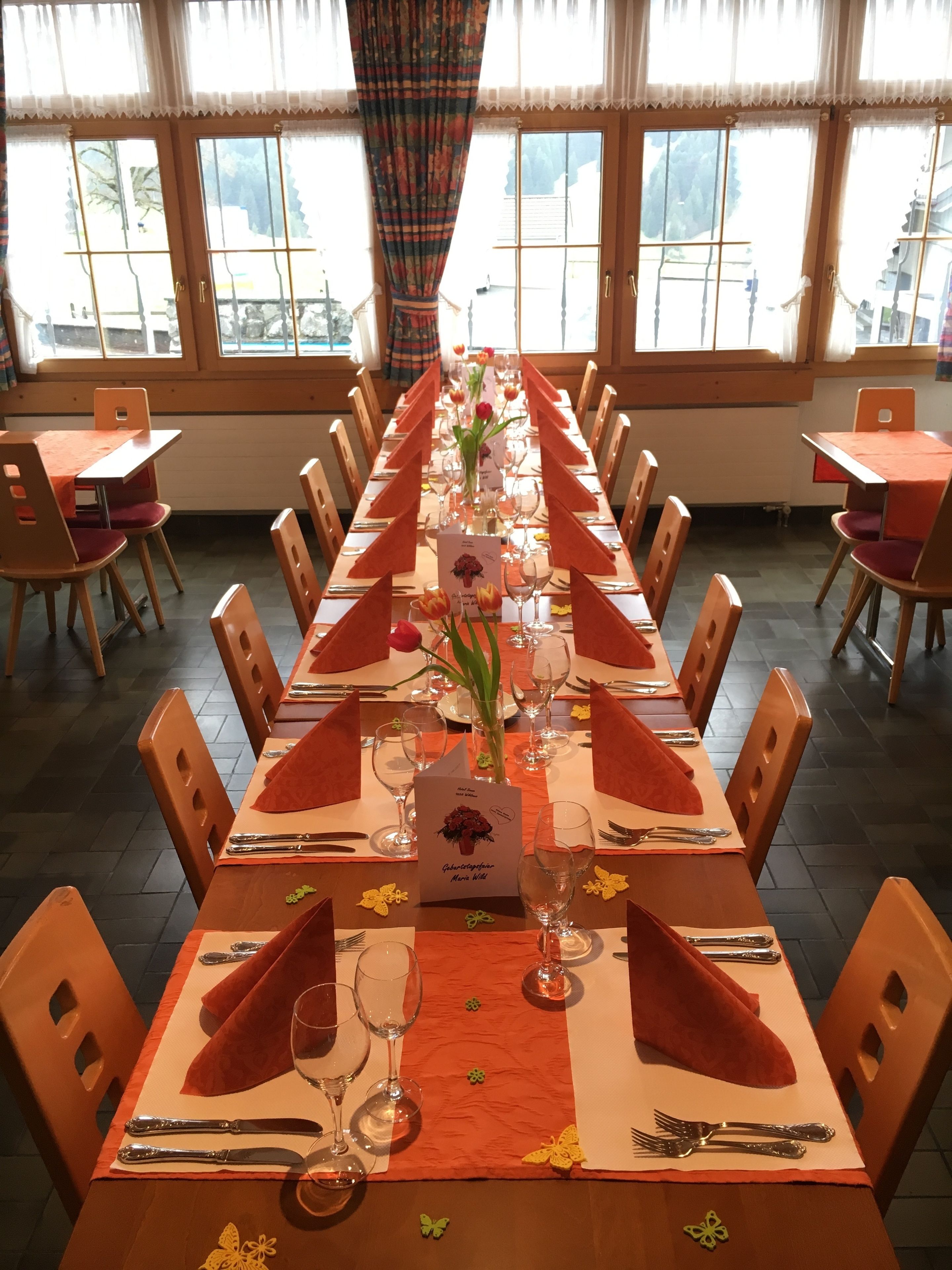Une longue table à manger, entourée de chaises, un vase rempli de fleurs et un menu.