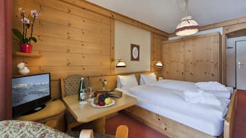 Habitación de hotel con decoración de madera, una cama, un televisor, una mesa con fruta, una planta y un cuadro colgado en la pared.
