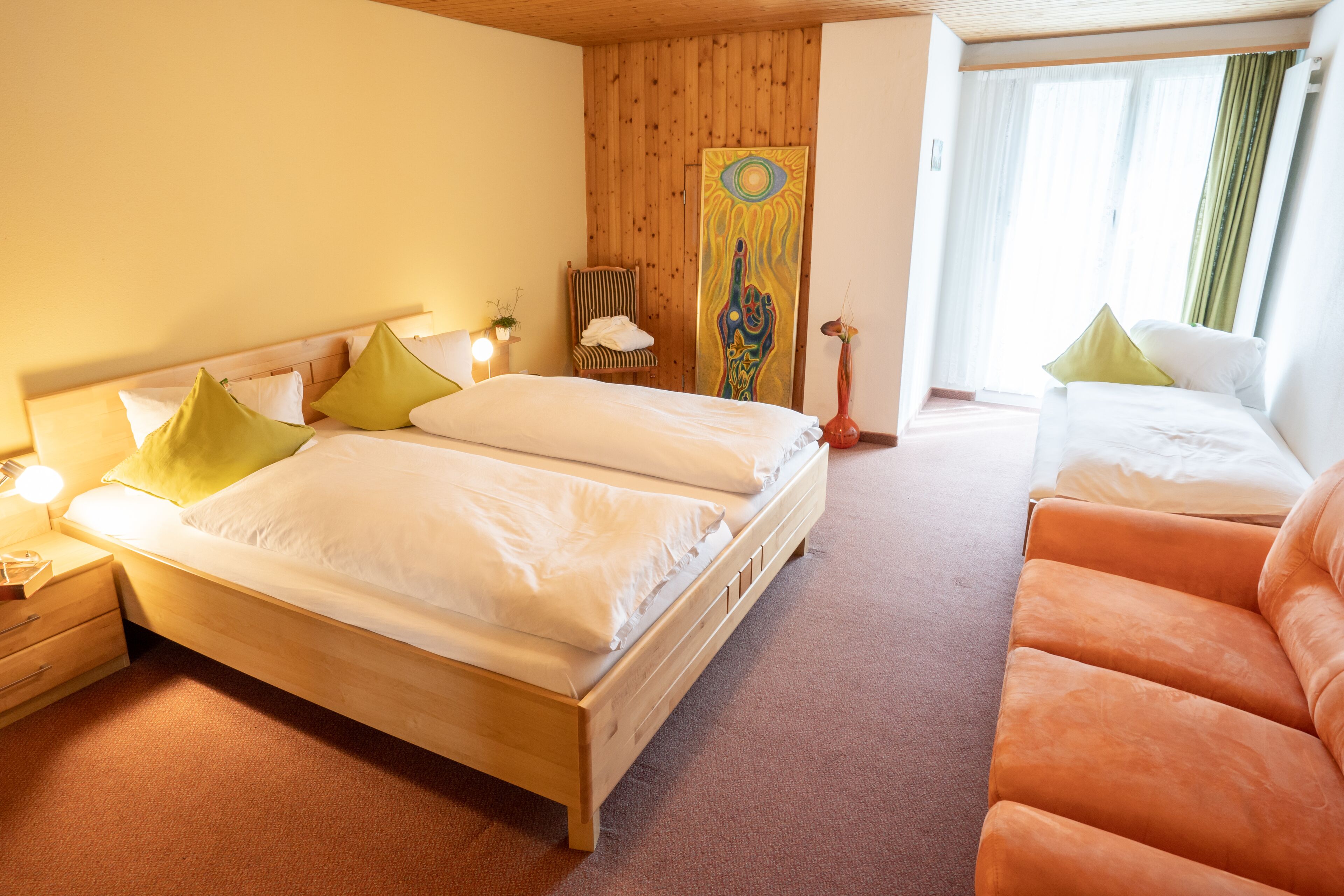 Une chambre d’hôtel avec un lit en bois, une table de chevet en bois, une chaise et un tableau au mur.