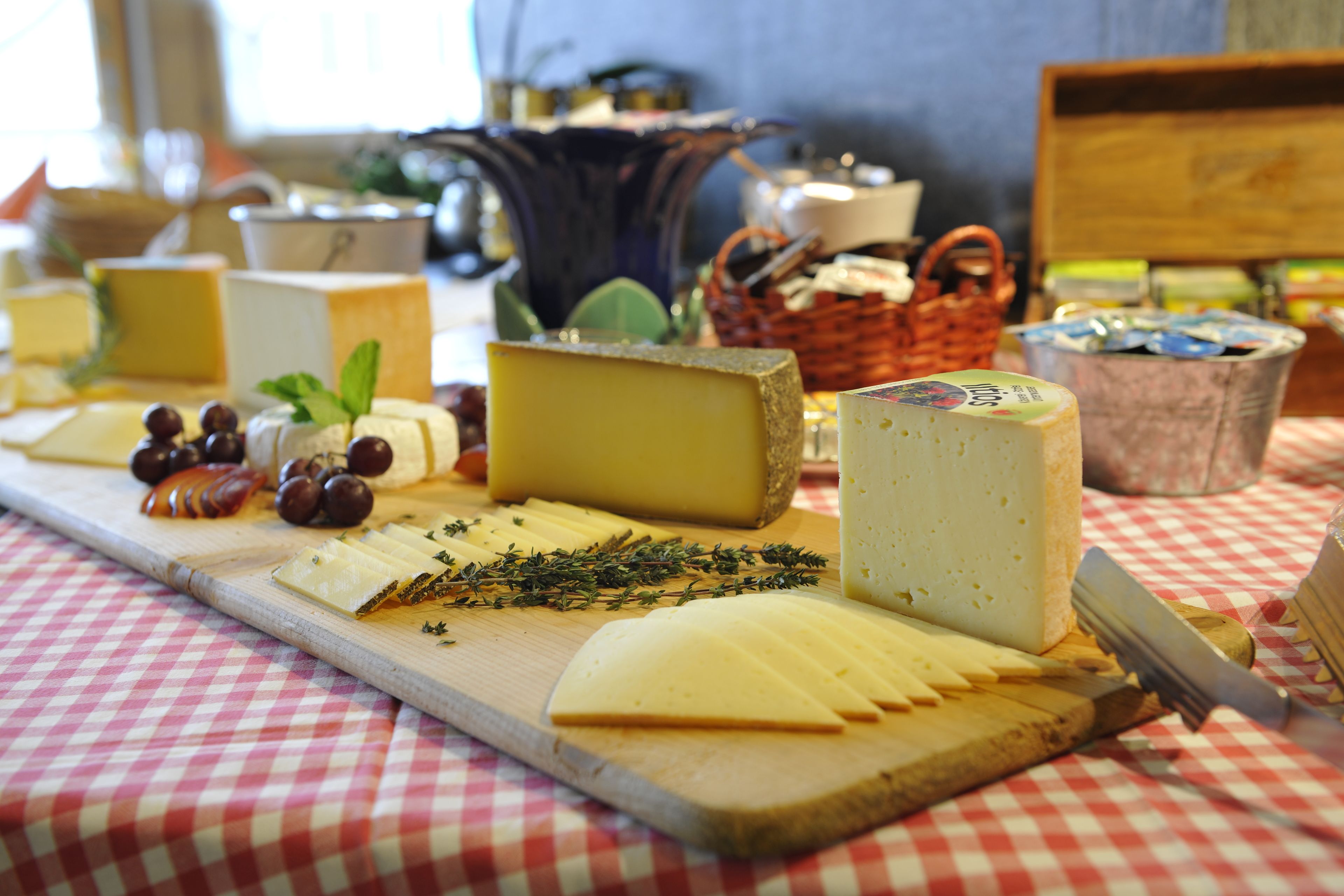 Assortimento di formaggi e uva su un tagliere di legno, con una tovaglia a scacchi sotto.