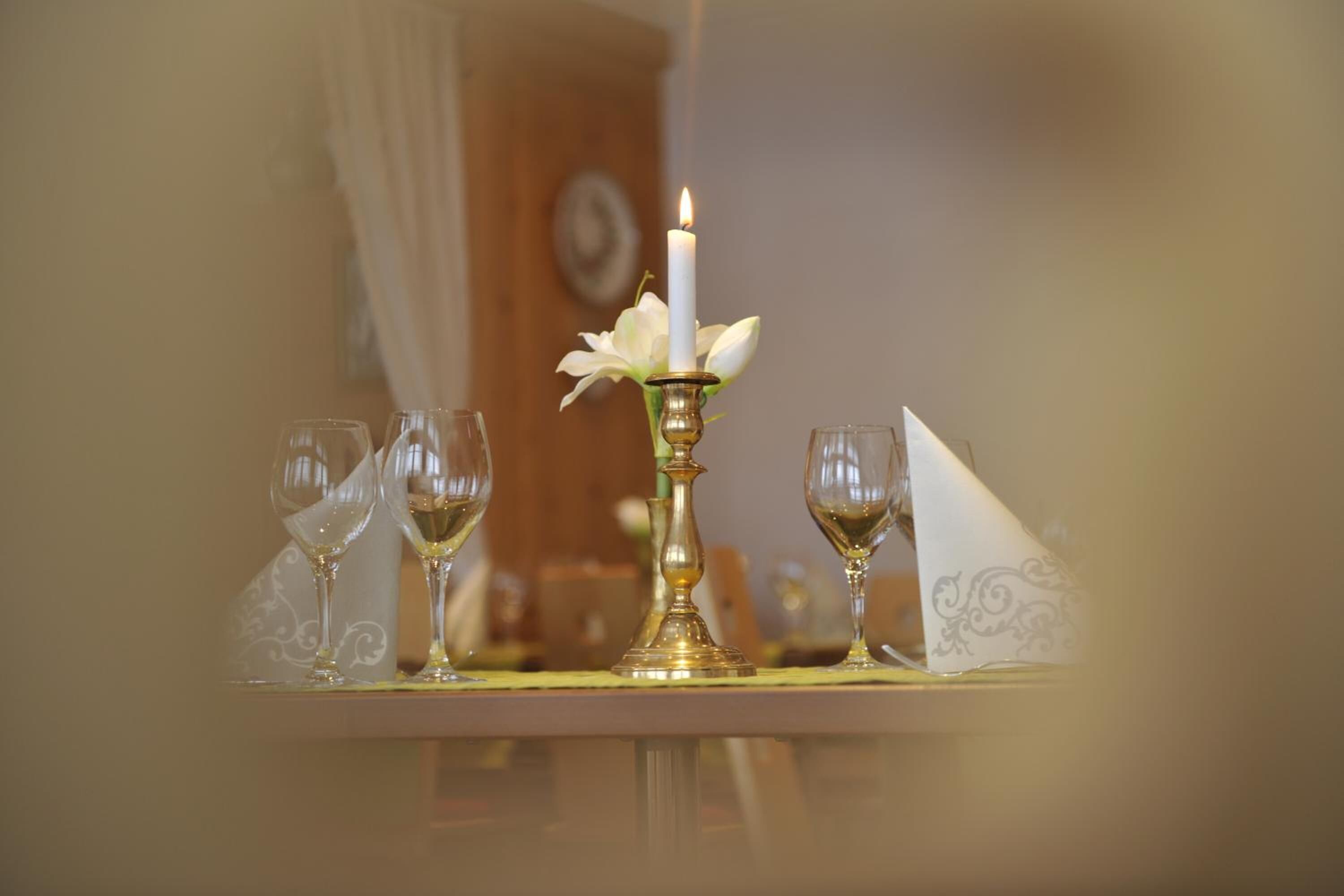 A table with a lit candle, a white flower, and three wine glasses.