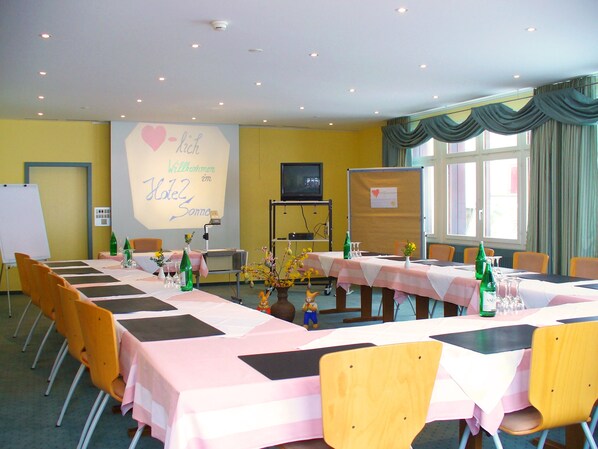 Une salle de conférence avec des tables disposées pour une réunion, équipée de chaises, de tables et d’un écran de projection.