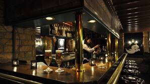 A bar area with a bartender preparing drinks, shelves with bottles, and stools. - Hotel Sonne (Wildhaus-Alt St. Johann)