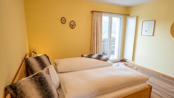 A double bed with white and dark gray linens, a wooden headboard, and a window with curtains.