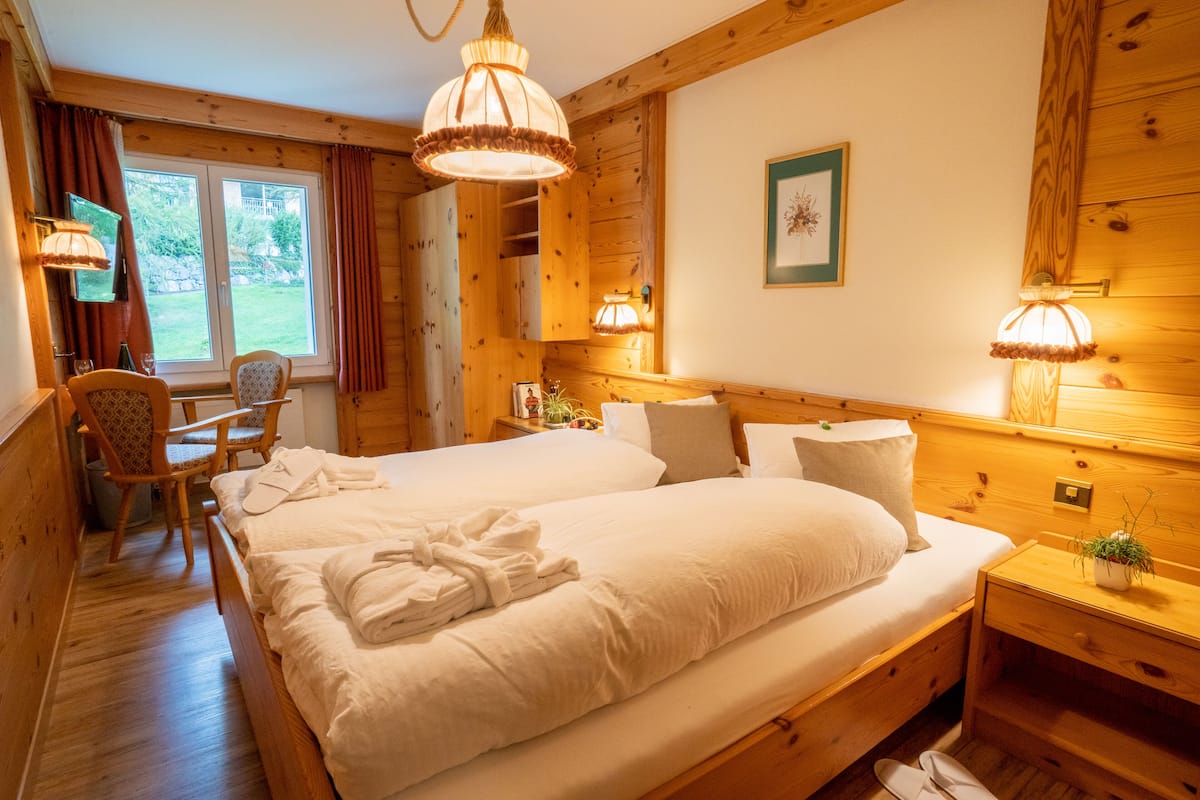 Une pièce chaleureuse en bois, avec un grand lit, une chaise, une petite table et une fenêtre avec des rideaux.