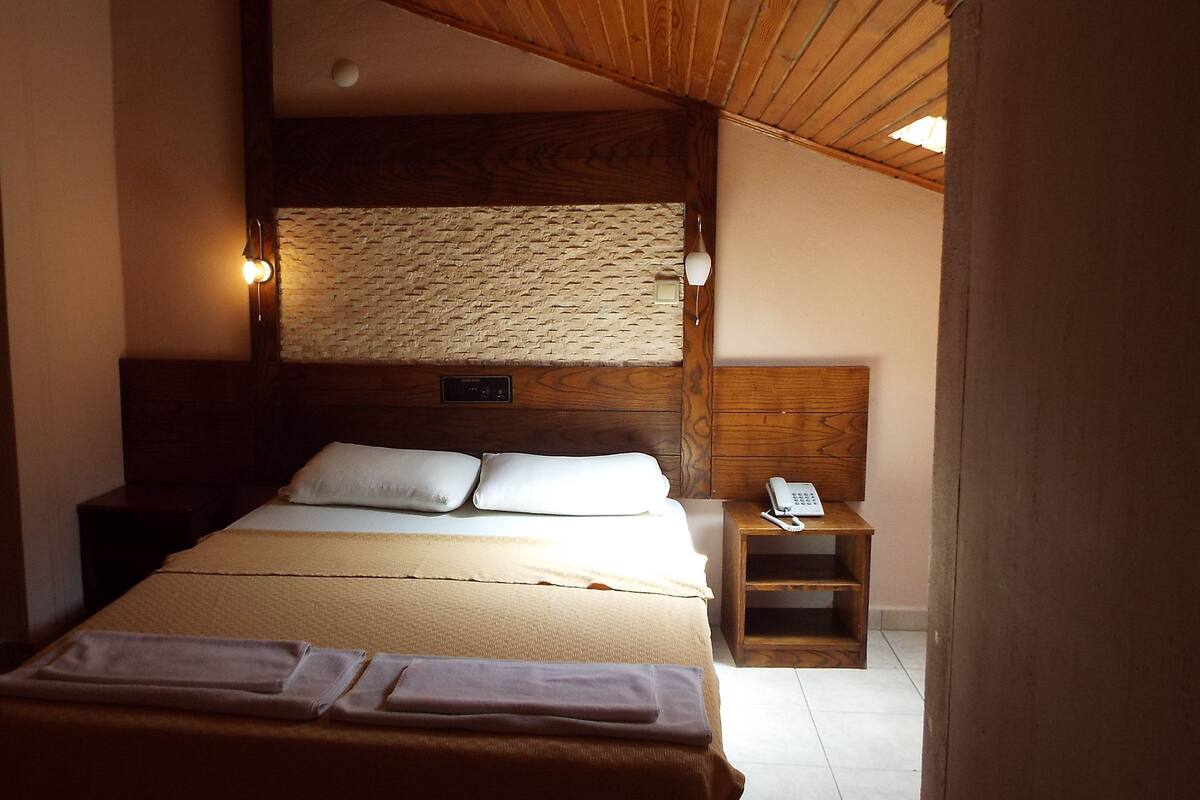 A bedroom with a wooden headboard, a stone accent wall, a bedside table with a phone, and neatly made beds.
