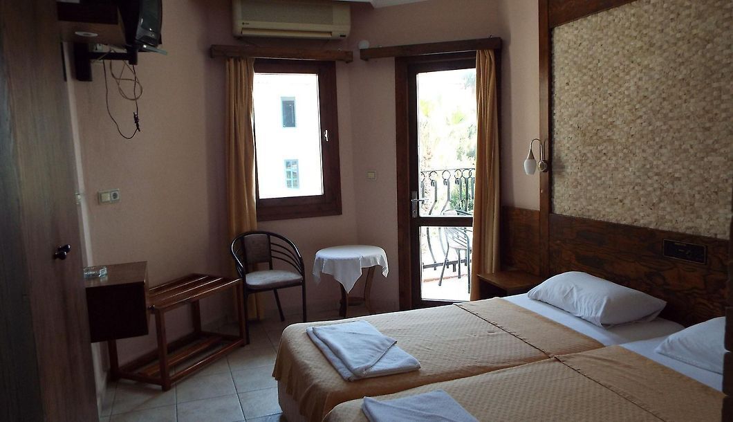 A hotel room with two beds, a small table, a chair, and a window with curtains.