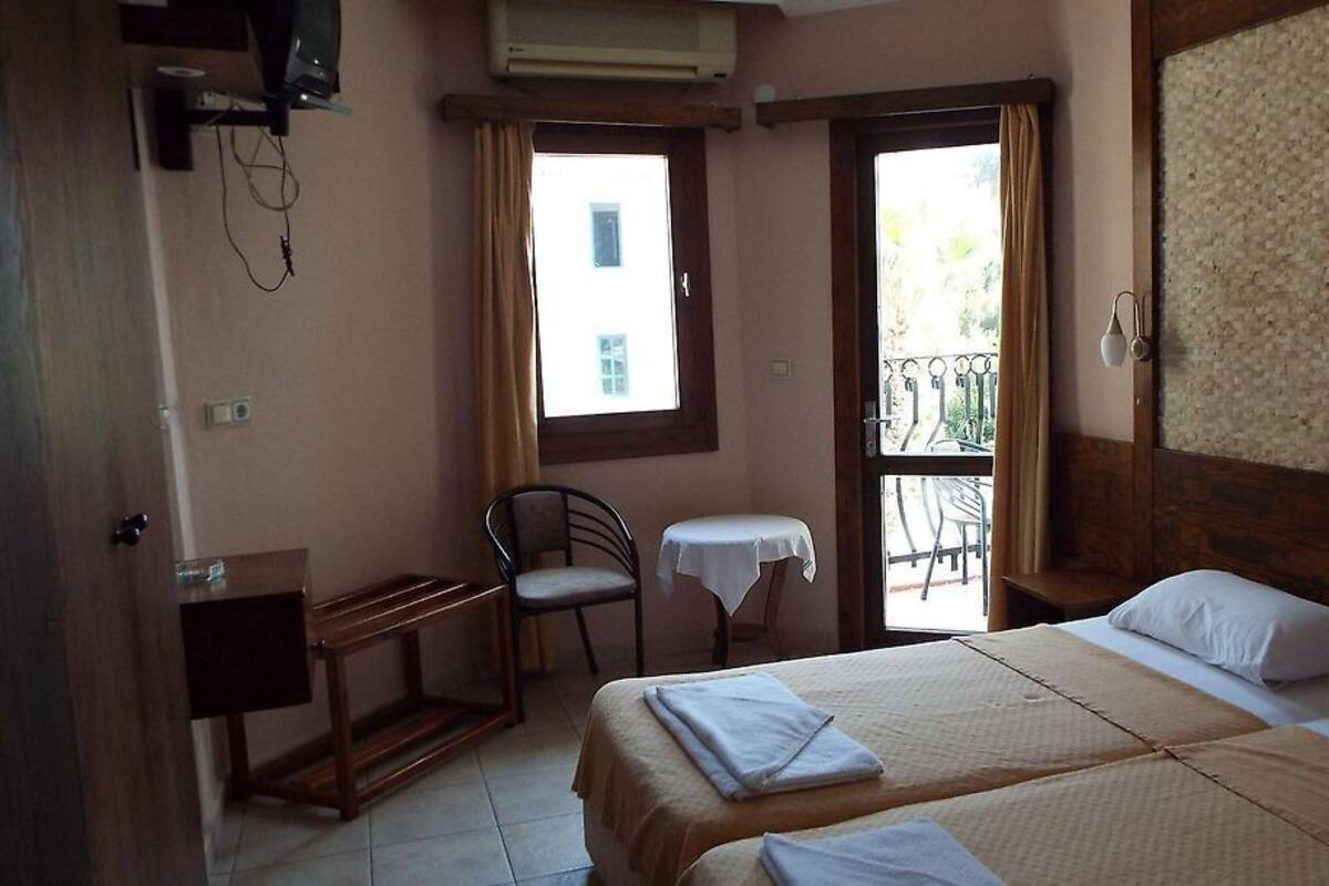 A hotel room with two beds, a small table, a chair, and a window with curtains.