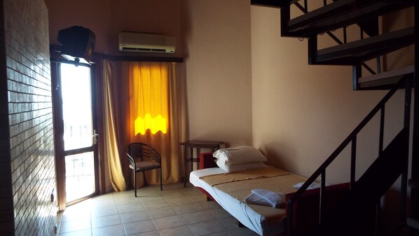 A small, dimly lit room with a single bed, a chair, a small table, and a staircase. - Area Hotel (Fethiye)