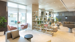 A modern hotel lobby with seating areas, a glass partition with shelves, and a view of the city. - Hotel Gracery Seoul (Seoul)
