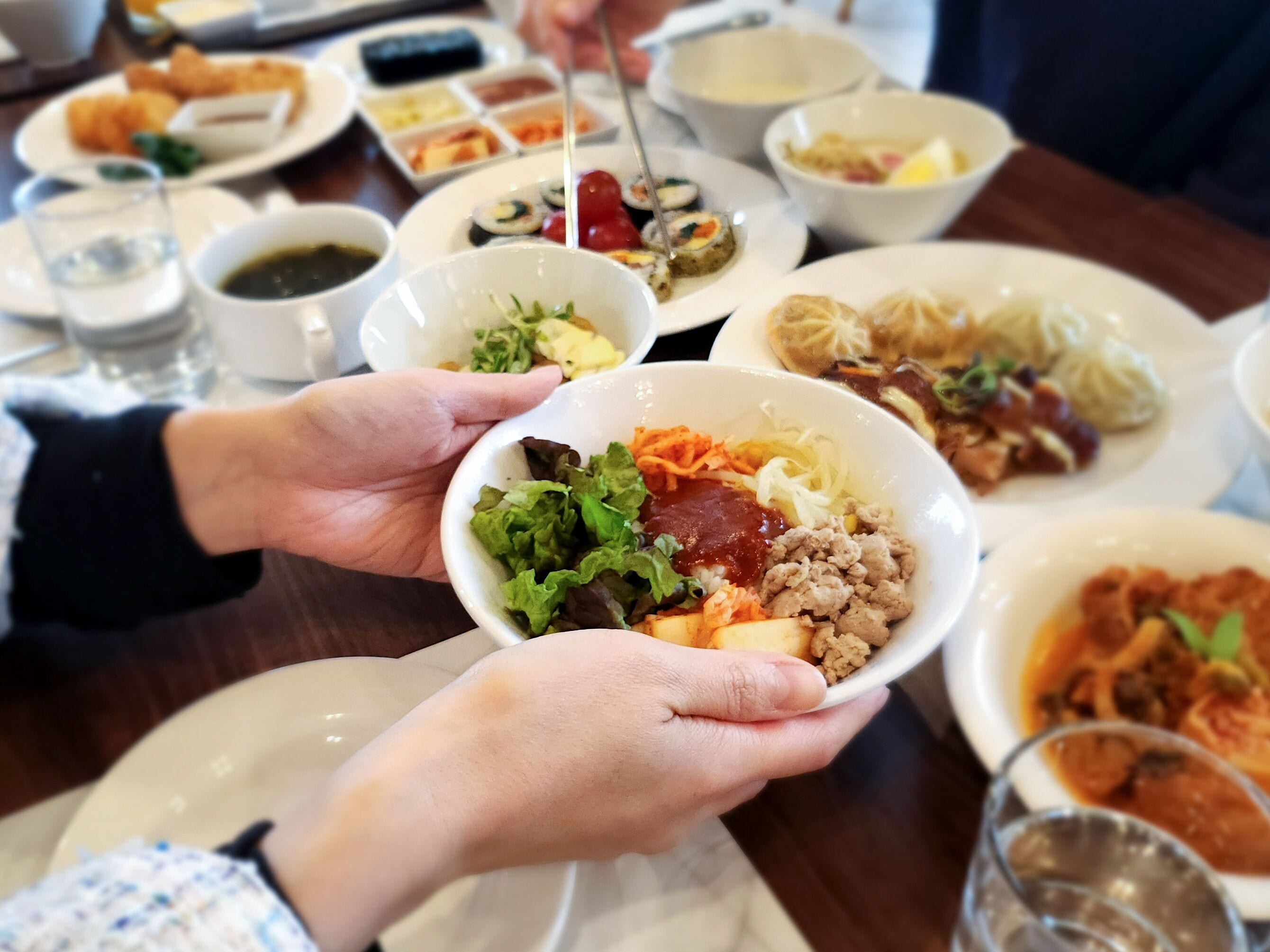 Une table dressée avec différents plats, notamment des sushis, des salades composées et un verre d’eau.