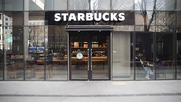 Una tienda Starbucks con fachada de vidrio moderna, área de asientos en el interior y vista despejada al interior a través del vidrio.