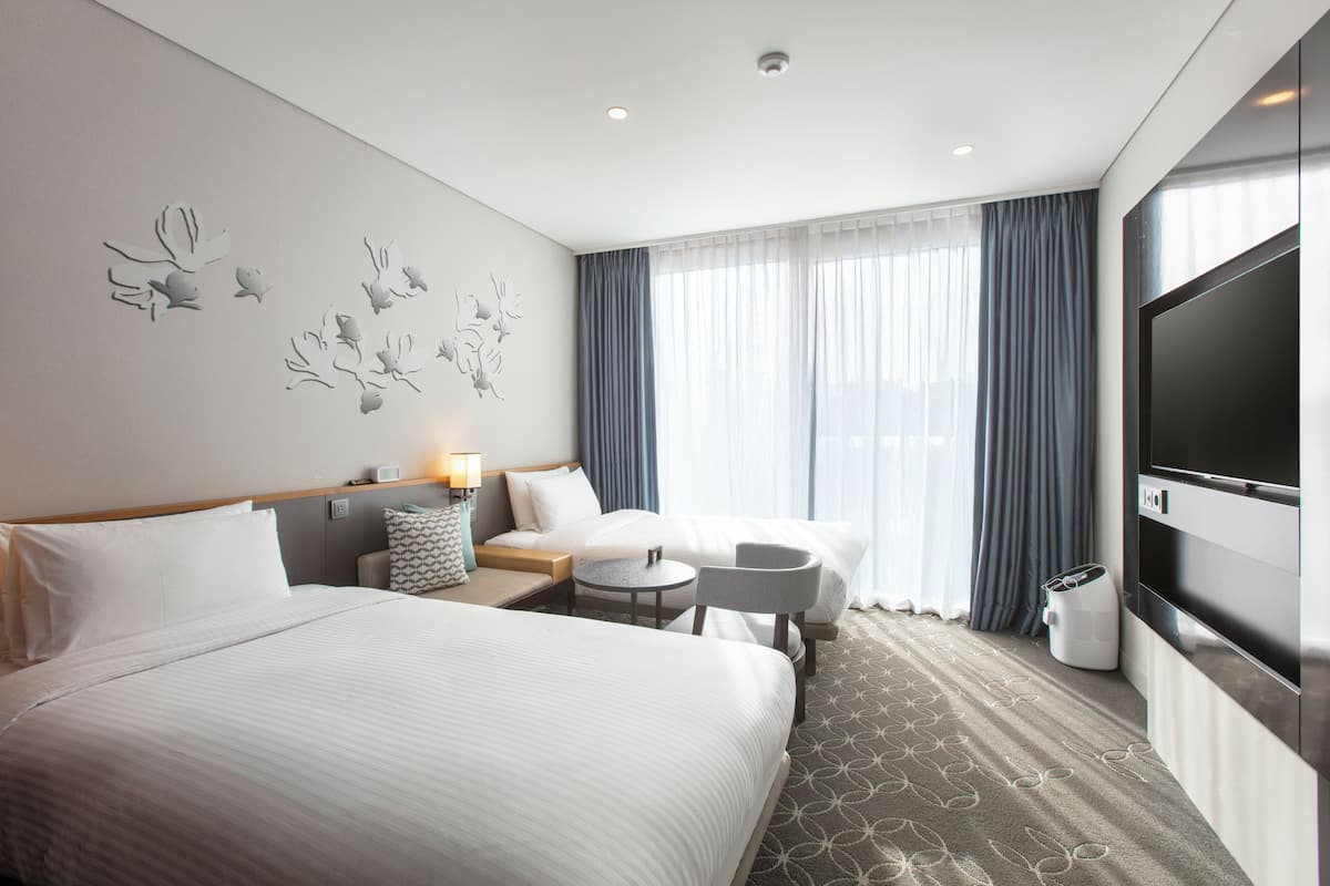Une chambre d’hôtel avec un grand lit, un canapé, une petite table, une télévision et une fenêtre avec des rideaux.