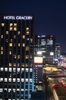 Un edificio de hotel moderno y alto, con ventanas iluminadas y un cartel llamativo que dice 'HOTEL GRACERY'.