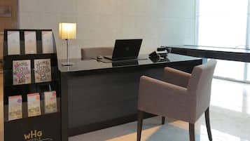 Un comptoir d’accueil d’hôtel avec un ordinateur portable, une lampe et une chaise. Des brochures sont disposées sur le côté gauche.