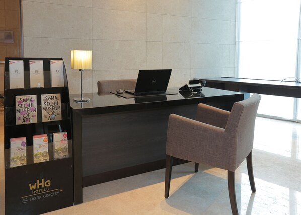Un mostrador de recepción de hotel con una computadora portátil, una lámpara y una silla. Hay folletos a la izquierda.
