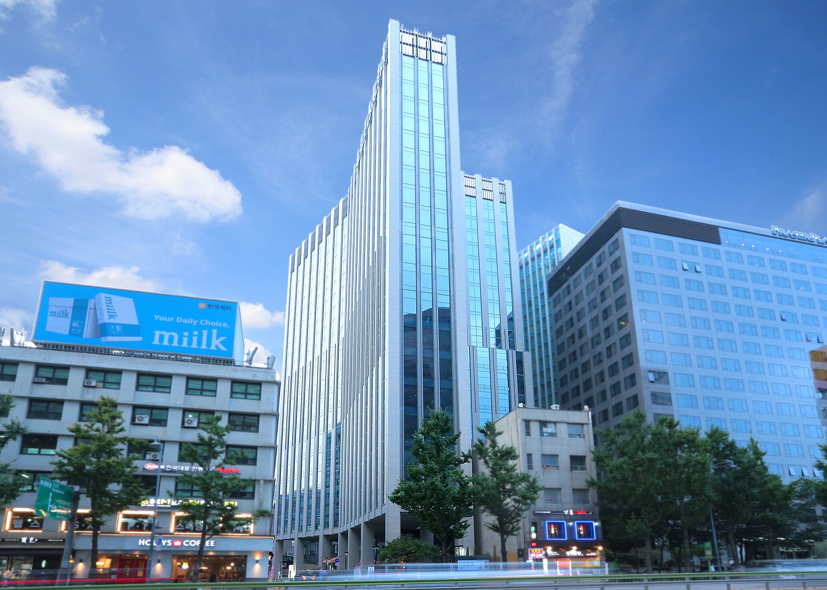 A modern high-rise building with a prominent glass facade, surrounded by other commercial buildings and a clear sky.