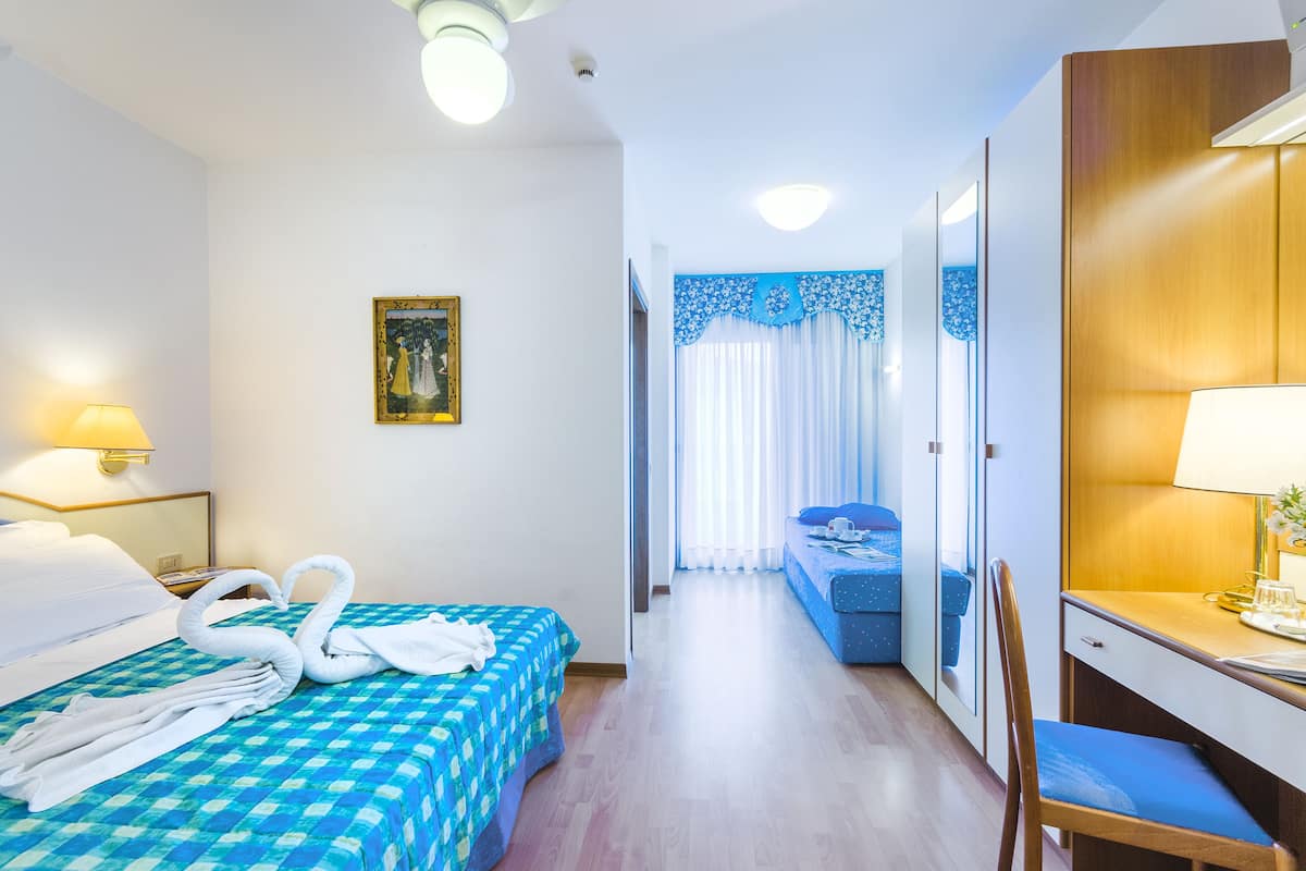 A hotel room with a bed, a desk, a chair, a lamp, and a window with curtains.