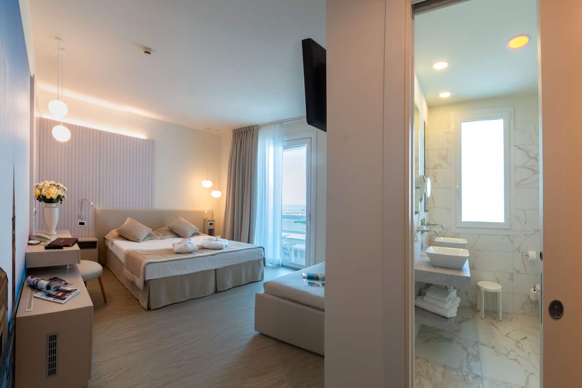 A modern hotel room with a bed, bedside table, lamp, and a view of the city.