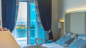 A hotel room with a bed, a nightstand, a lamp, and a view of the beach through the window. - Hotel Panoramic (Caorle)