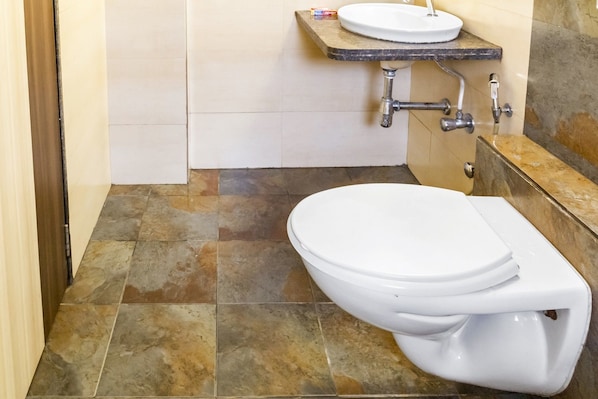A bathroom with a white toilet, a sink with a marble countertop, and a tiled floor.