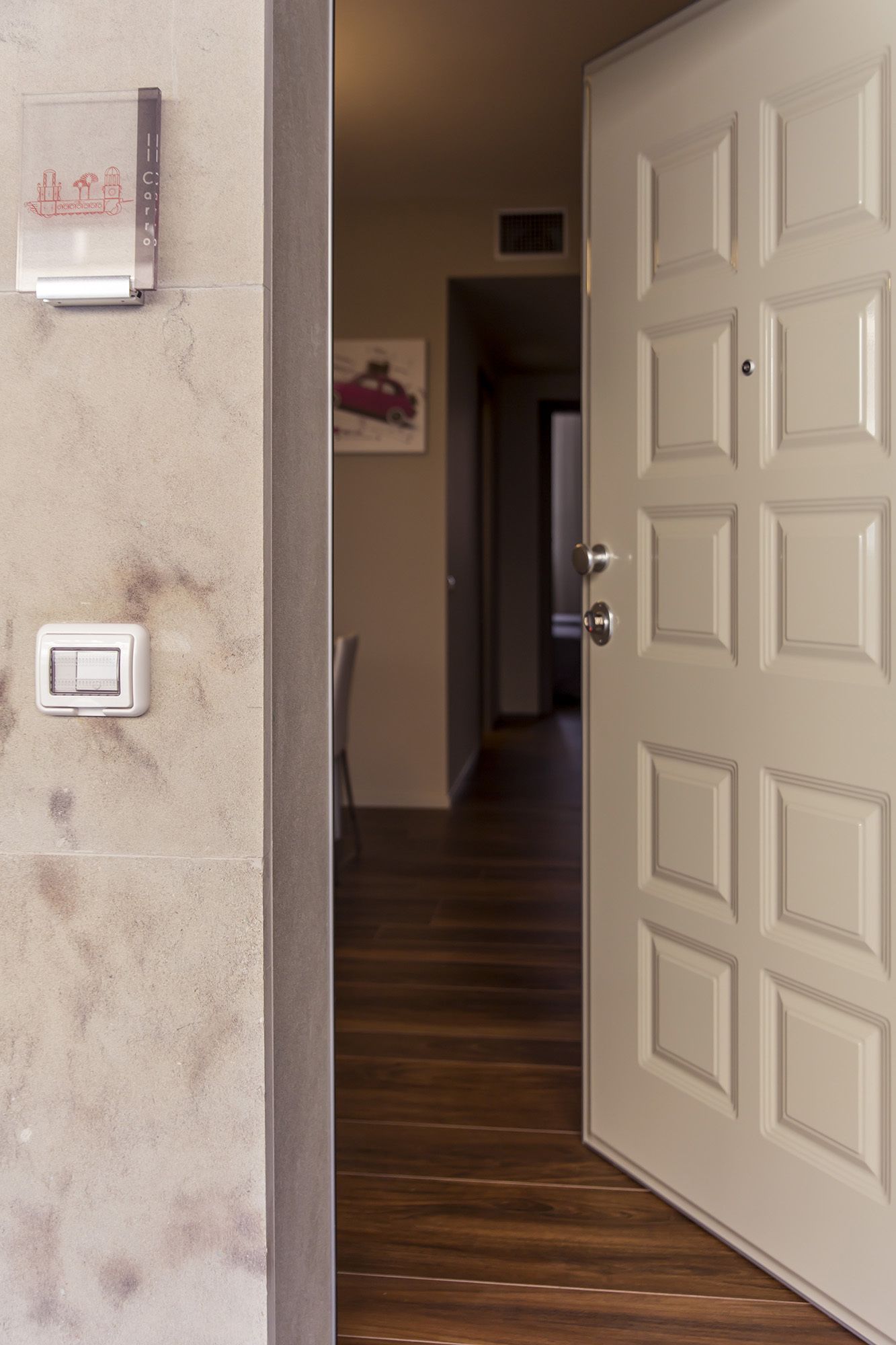 A hallway with a wooden floor, a white door, and a wall-mounted thermostat.