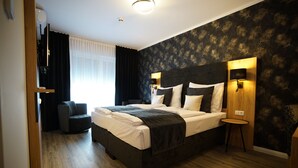 Une chambre à coucher moderne avec un grand lit, un papier peint à motifs foncés et une petite table de chevet avec une lampe.