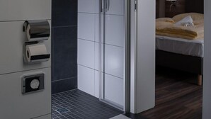 Une chambre d’hôtel moderne dotée d’un dressing, d’un lit avec une tête de lit et d’une salle de bain équipée d’un porte-rouleau de papier toilette.