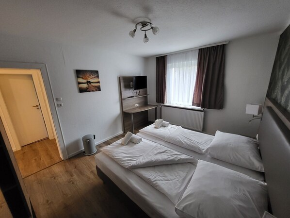 Una habitación de hotel con dos camas, televisión, un cuadro y una ventana con cortinas.