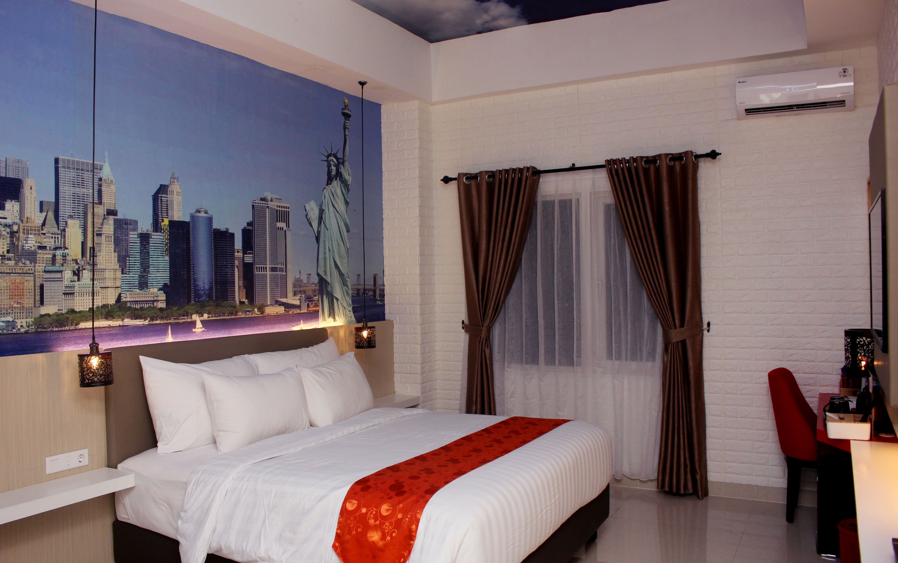 A hotel room with a bed, a desk, a chair, a cityscape mural, and a window with curtains.