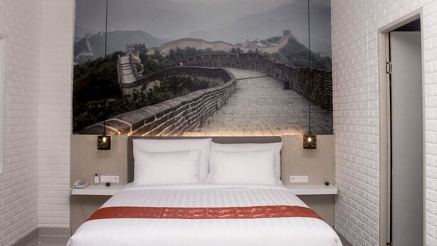 A hotel room with a large mural of the Great Wall of China on the wall behind the bed.