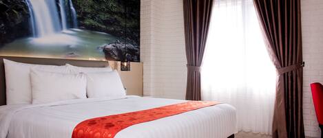 A hotel room with a large bed, white bedding, a red throw, a mural of a waterfall, and brown curtains.