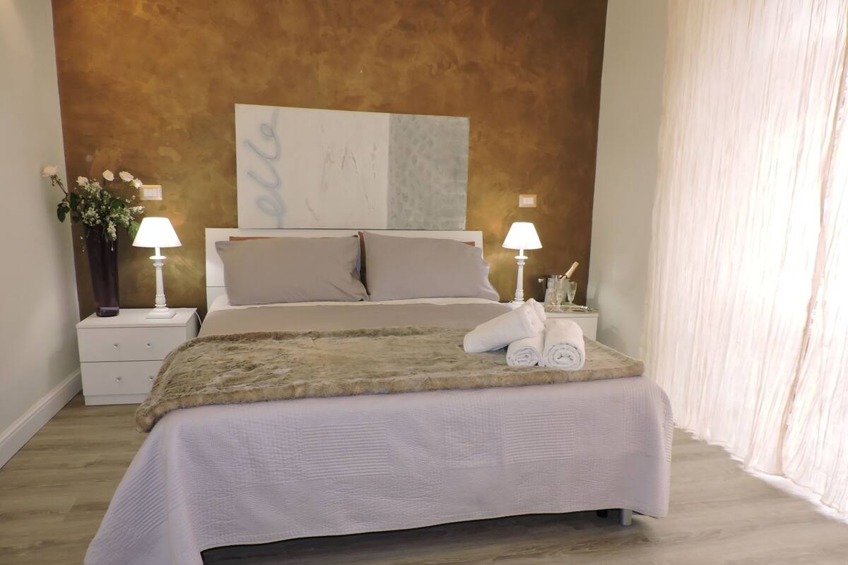 A neatly made bed with a fluffy blanket, two bedside lamps, and a vase with flowers on a nightstand.