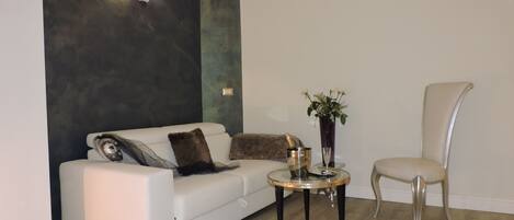 A modern living room with a white sofa, a glass coffee table, and a high-backed chair.
