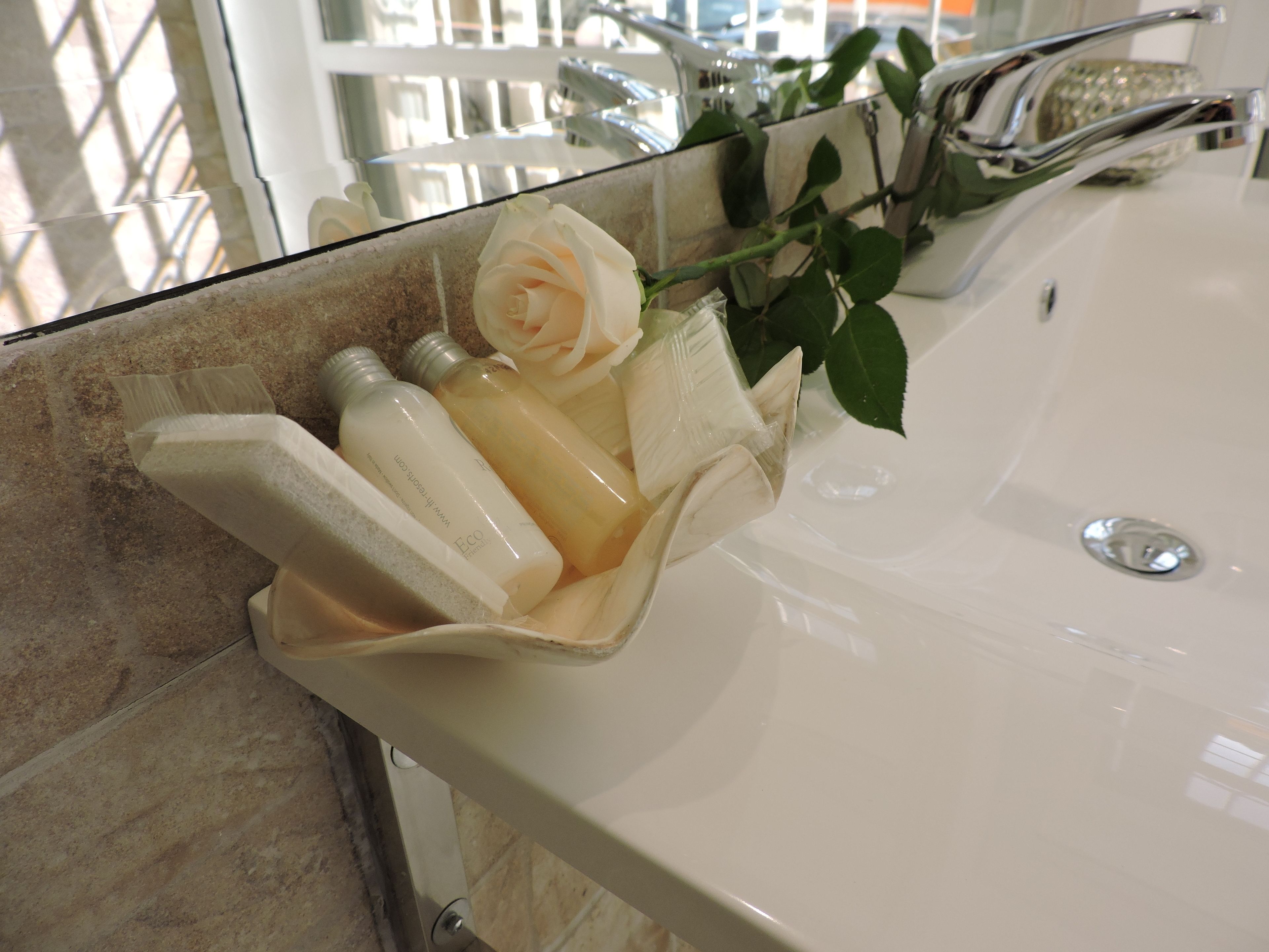 A bathroom sink with a glass container holding a white rose and two bottles.