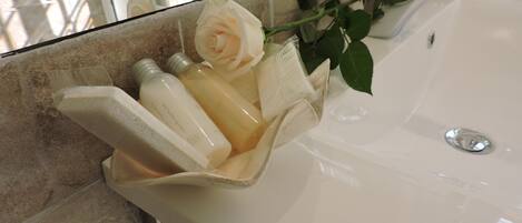 A bathroom sink with a glass container holding a white rose and two bottles.